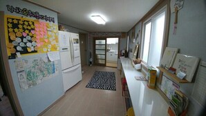 Eine Küche mit Kühlschrank, Mikrowelle und Spüle. An der Wand befinden sich Notizen und Zeichnungen, und es gibt ein Fenster mit Vorhängen.