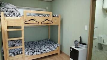 A bunk bed room with zebra-patterned bedding, a small refrigerator, and a bathroom visible through a glass door.