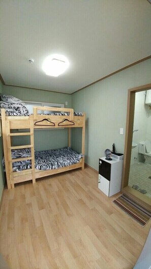 A bunk bed room with zebra-patterned bedding, a small refrigerator, and a bathroom visible through a glass door.