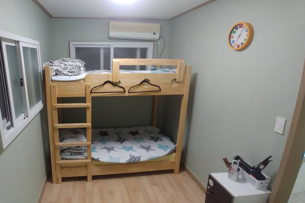 A bunk bed with a wooden ladder, a window with frosted glass, an air conditioner, and a wall clock.