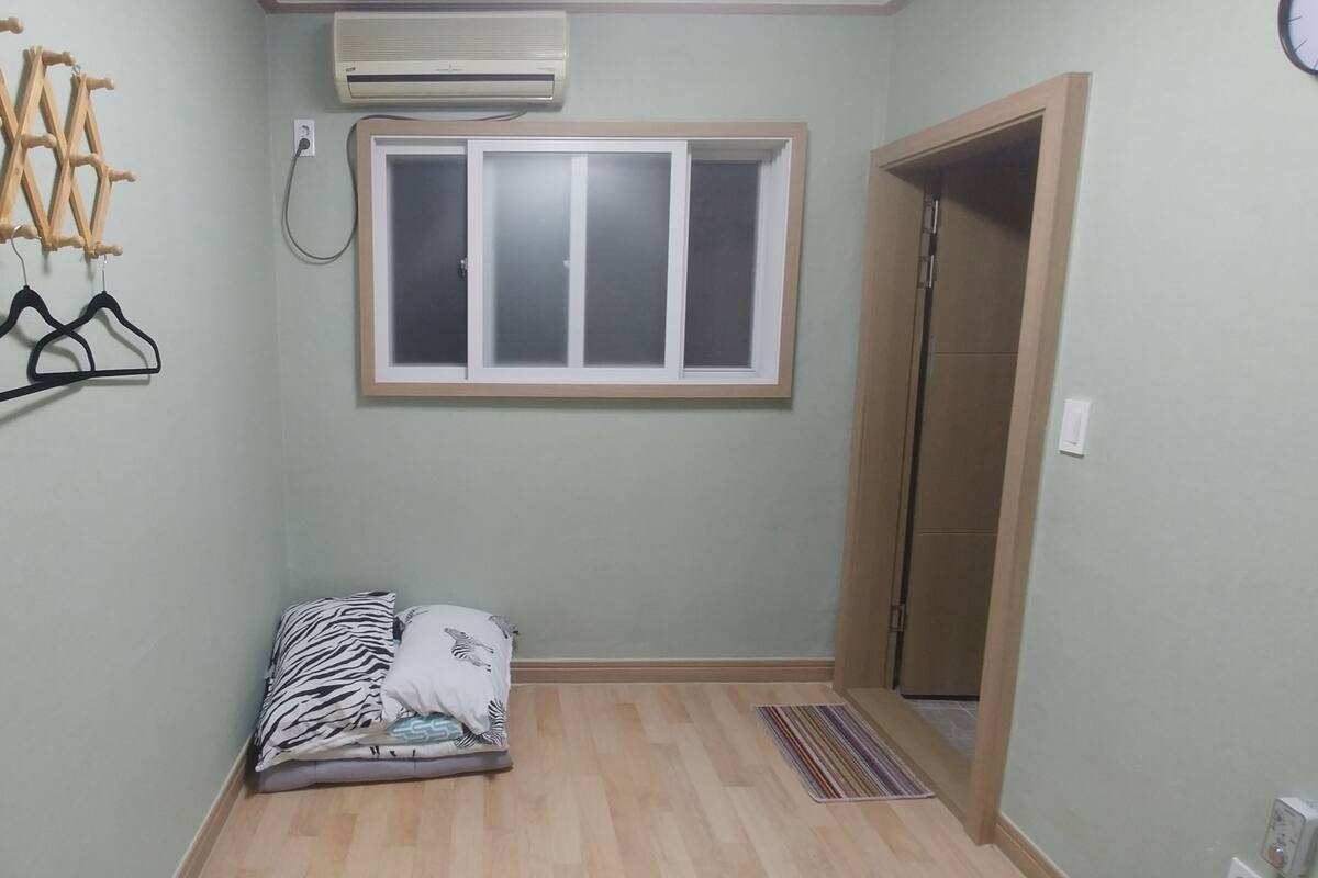 A small room with a bed, a window, an air conditioner, and a door.