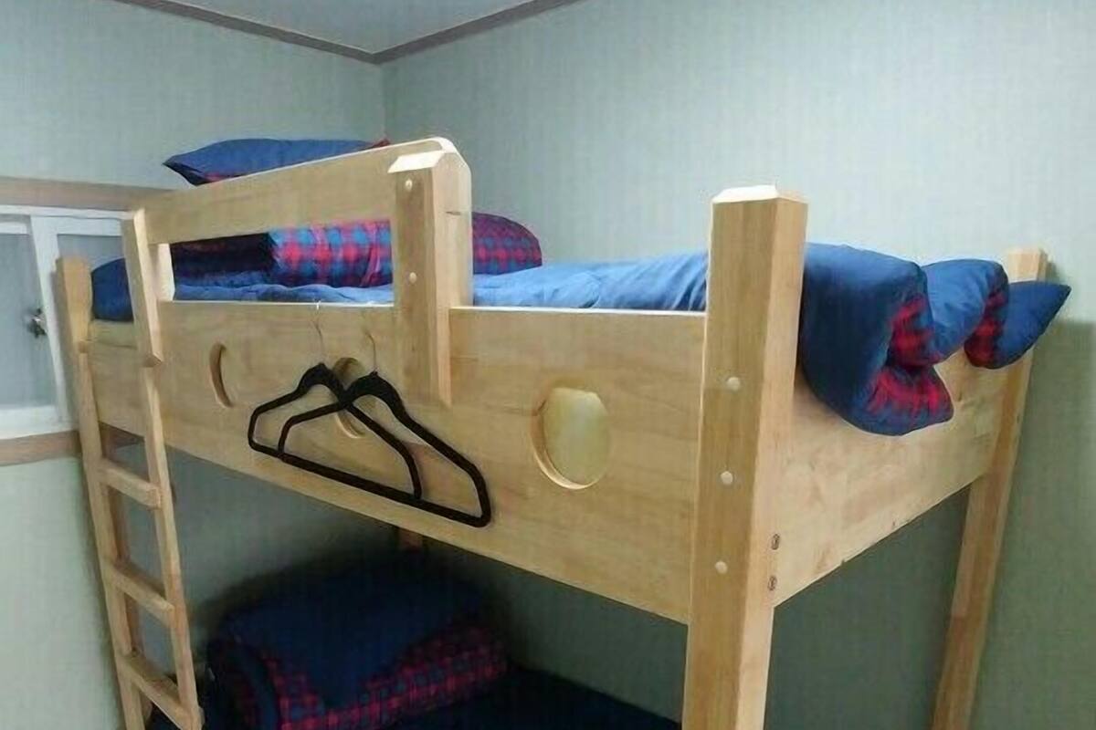 A bunk bed with a ladder, a small shelf, and a wall-mounted light fixture.