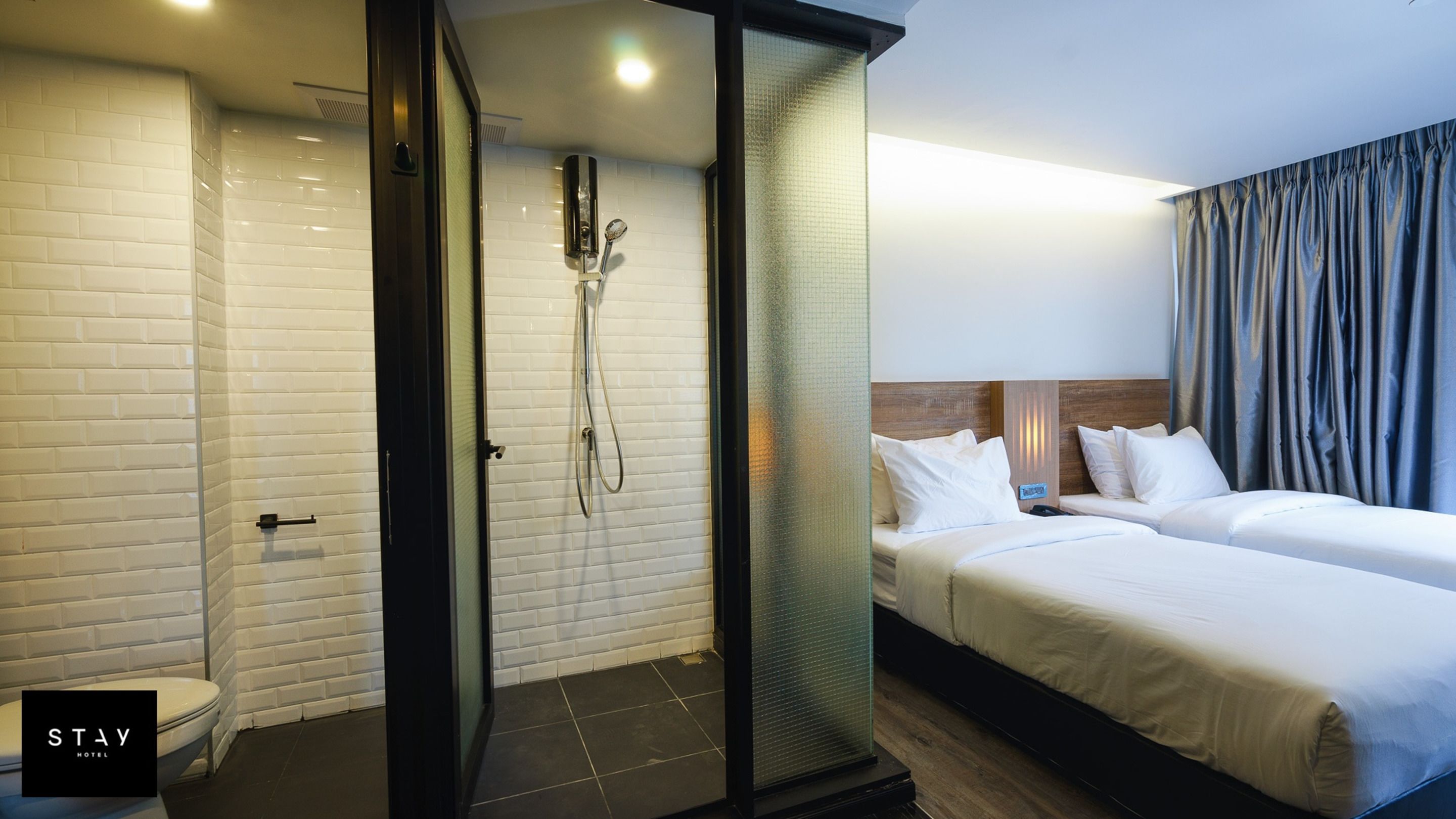 Habitación de hotel con ducha, dos camas, inodoro y zona de ducha con mampara de vidrio.
