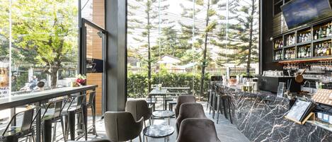 Un espace extérieur aménagé avec des tabourets de bar et des tables, un comptoir en marbre et une vue sur les arbres et les bâtiments.