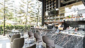 Una zona de bar moderna con mostradores de mármol, una variedad de botellas de licor y asientos con mesas y sillas redondas.