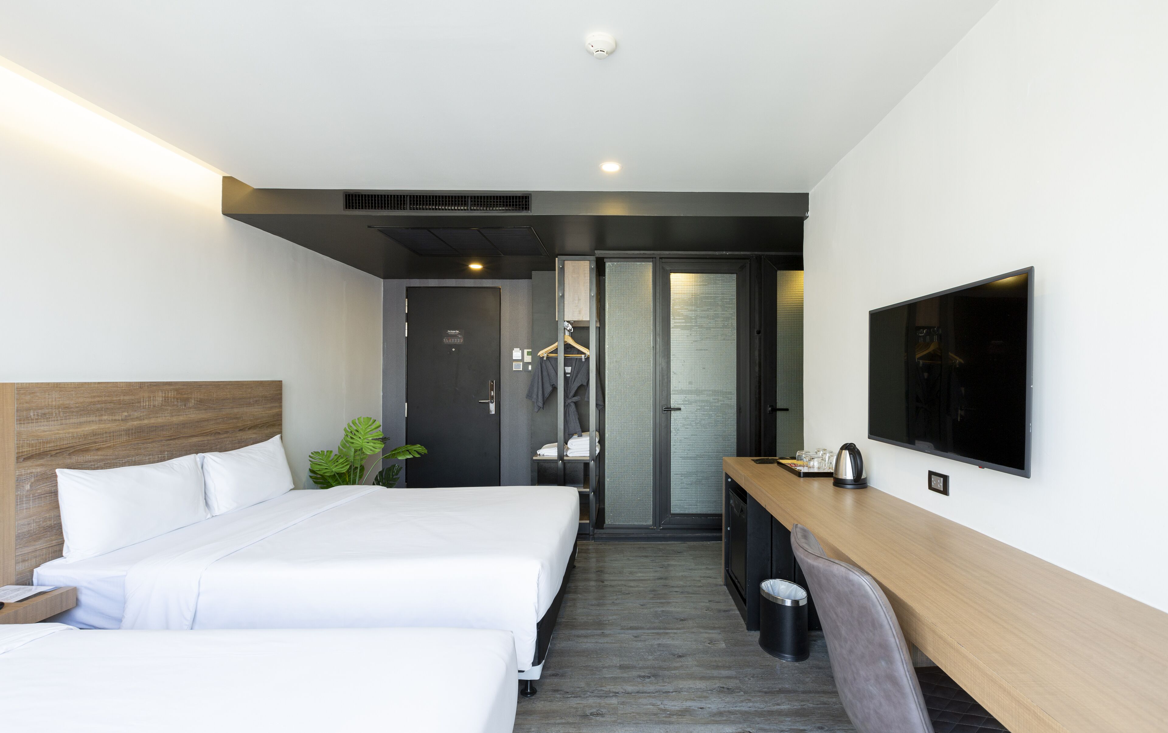 A modern hotel room with two beds, a desk, a TV, and a shower area.