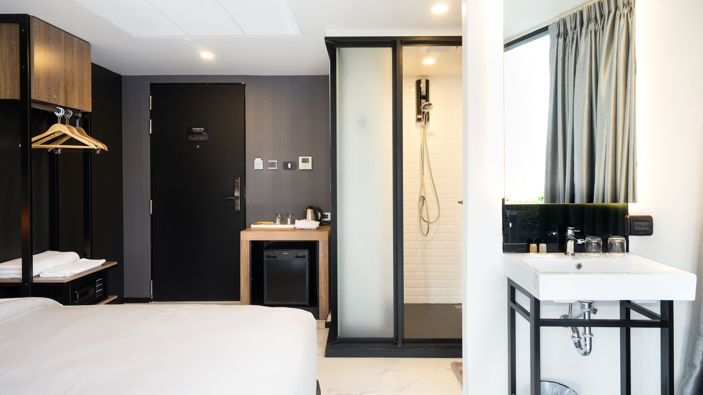 Moderni hotellihuone, jossa on sänky, pieni työpöytä, jossa on vedenkeitin, suihkutila sekä kylpyhuone, jossa on peili ja pesuallas.