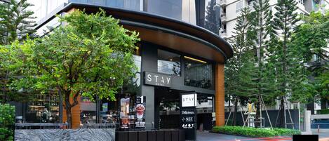 Un hotel moderno con fachada curva, restaurante visible y un letrero que dice 'STAY HOTEL'.