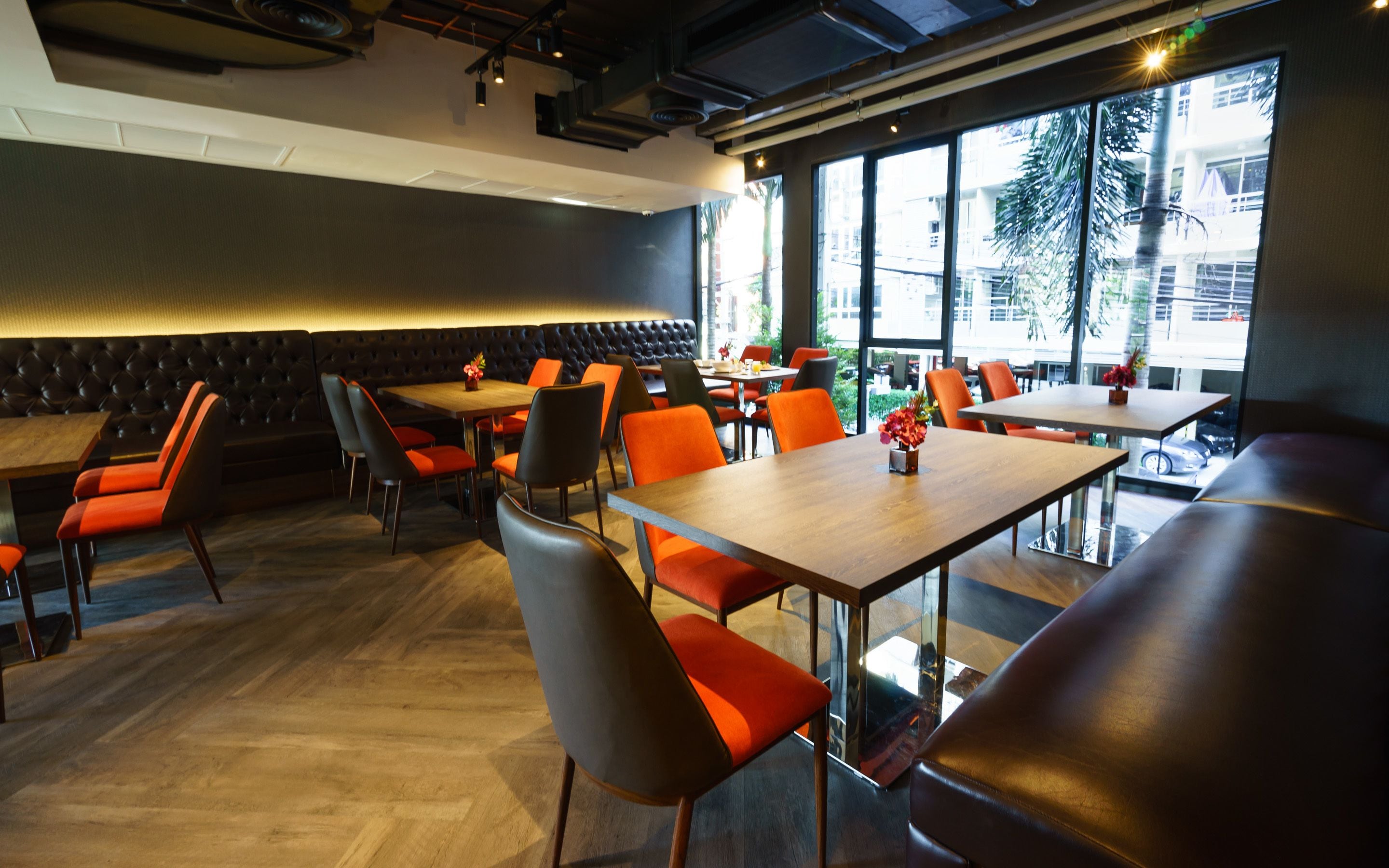 A modern restaurant with a mix of booths and tables, featuring a wooden floor and large windows offering a view of the outdoors.