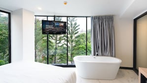 Un baño moderno con una bañera independiente, un ventanal con vistas a árboles y un televisor de pantalla plana montado en la pared.