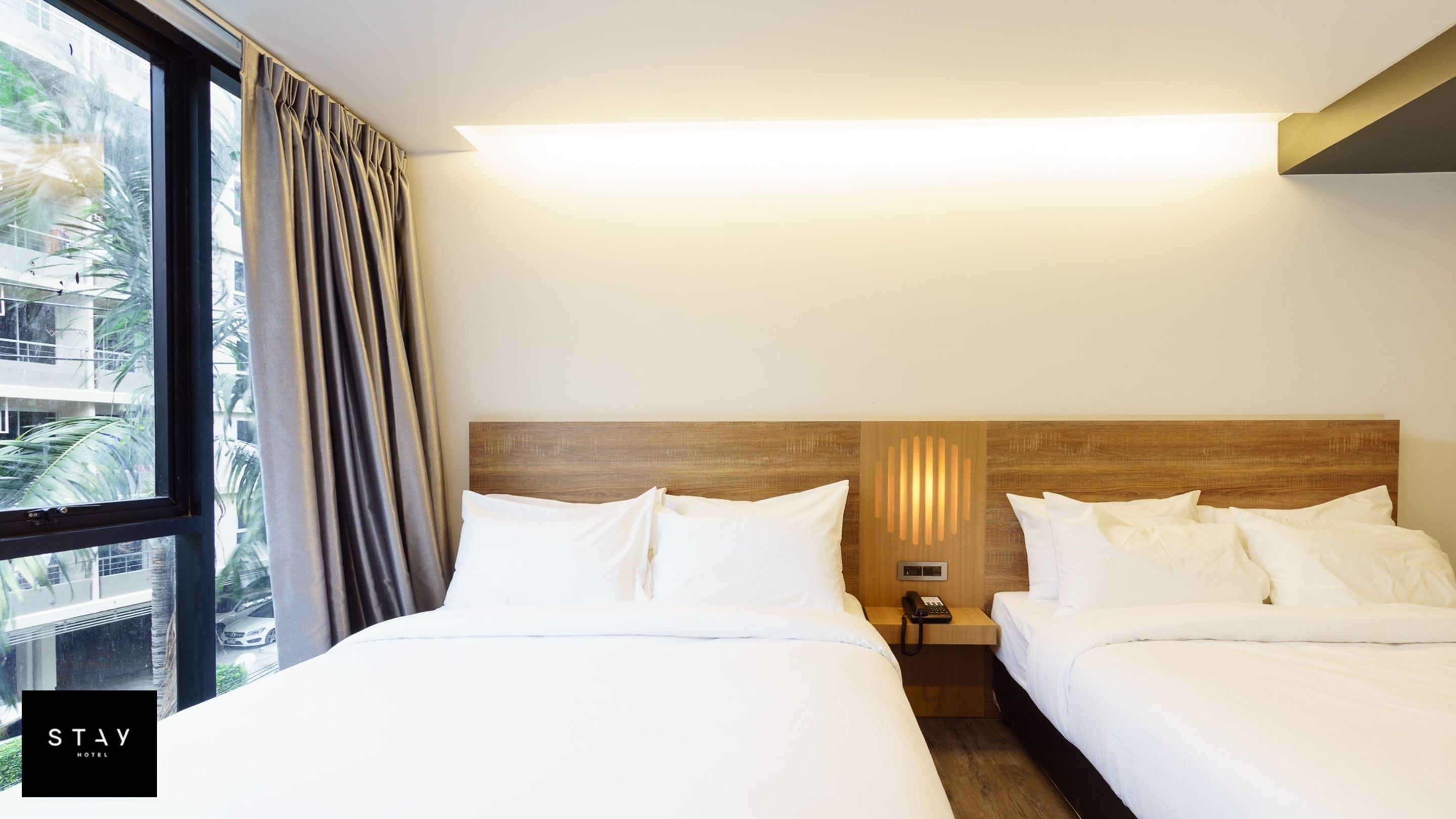 A hotel room with two beds, a nightstand with a phone, and a window with curtains.
