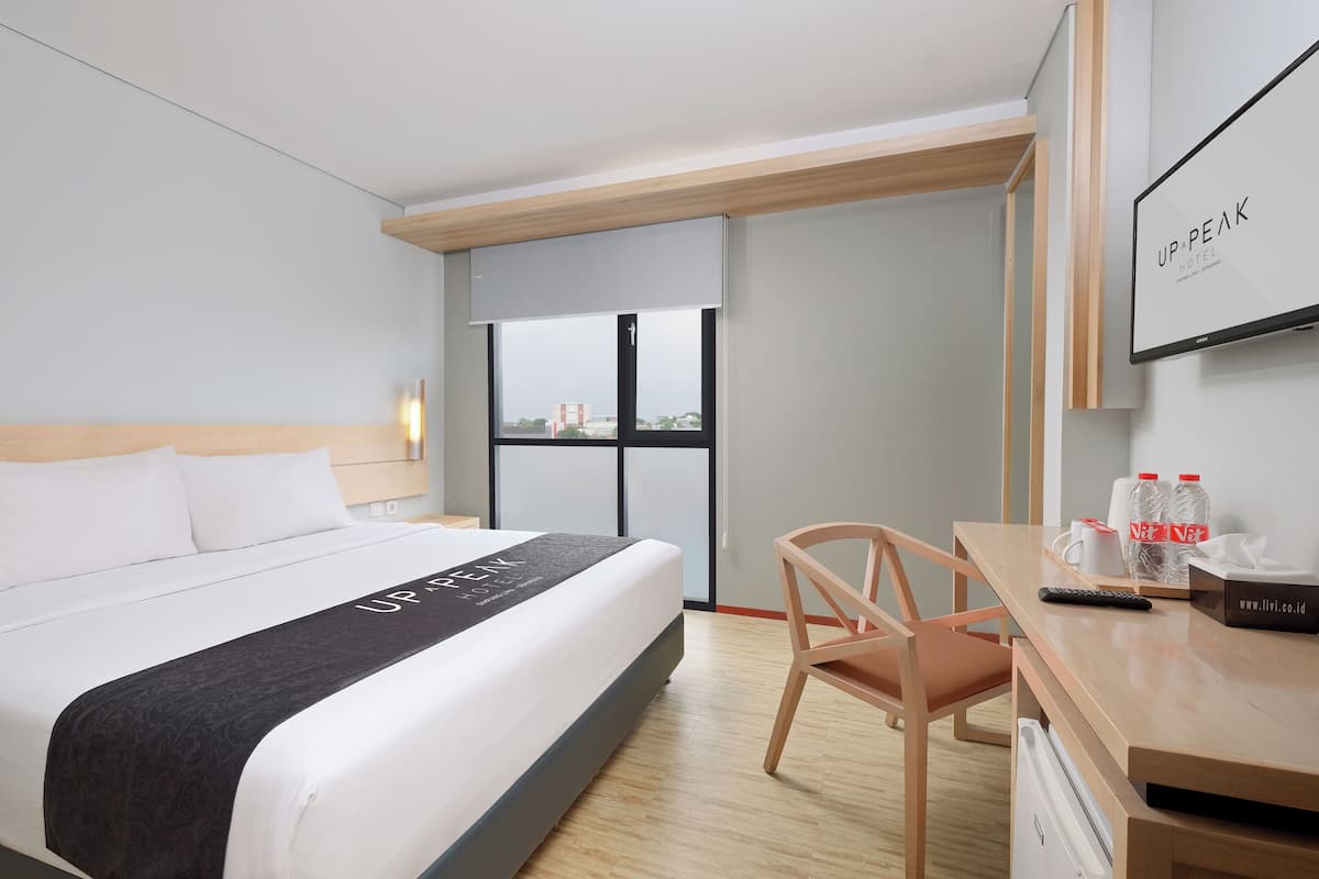 A hotel room with a bed, a desk, a chair, a TV, and a window with a view.