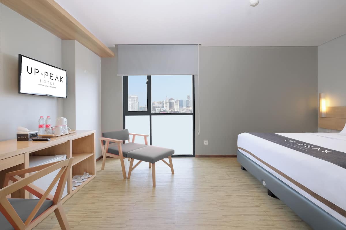A hotel room with a bed, a desk with a chair, a television, and a large window with a city view.
