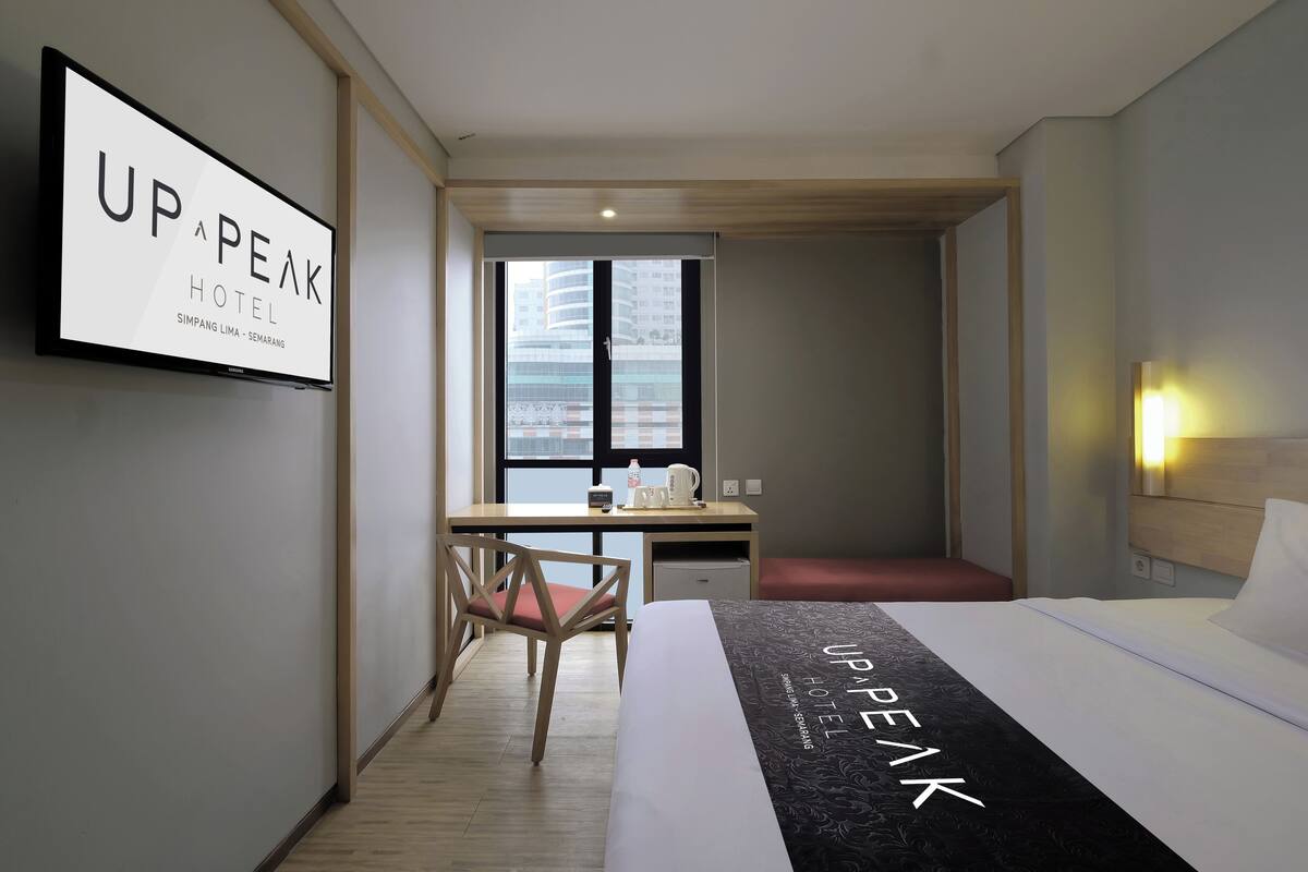 A hotel room with a bed, a desk, a chair, a TV, and a window with a city view.