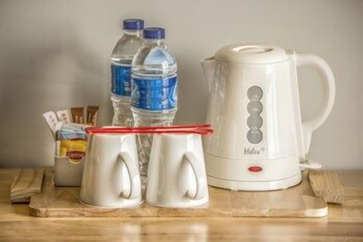 A kitchen area with a white kettle, two water bottles, and two mugs on a wooden surface.
