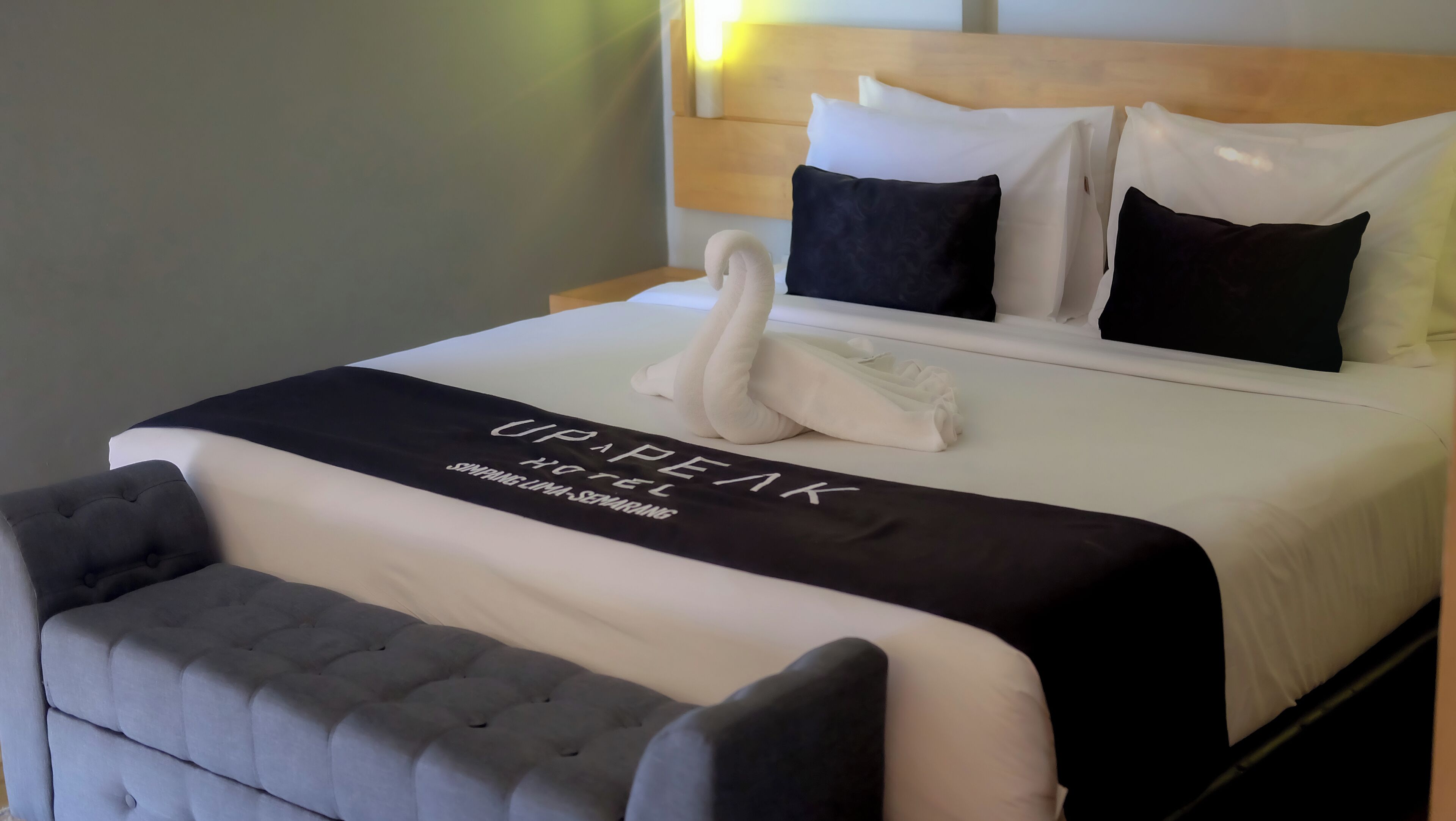 A neatly made bed with a swan-shaped pillow, a black and white bedspread, and a grey upholstered headboard.