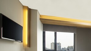 A modern room with a flat-screen TV mounted on the wall, a large window with a view of the cityscape, and a wooden beam ceiling. - Up-Peak Hotel Simpang Lima Semarang (Semarang)