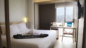 A hotel room with a bed, a desk with a laptop, a window with a city view, and a wall-mounted TV. - Up-Peak Hotel Simpang Lima Semarang (Semarang)