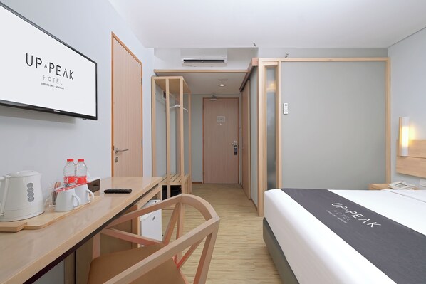 A hotel room with a bed, a desk with a coffee maker, a chair, and a TV displaying the hotel name.