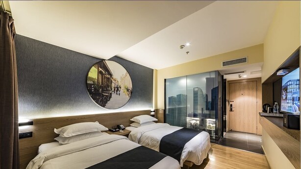 A hotel room with two beds, a large mirror, a cityscape view, a wooden door, and a small desk with a TV. - Hollyston Hotel of Chengdu (Chengdu)