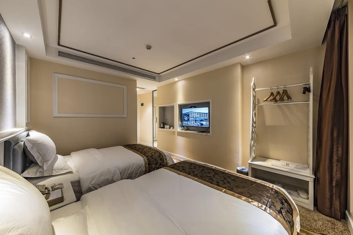 A hotel room with two beds, a TV, a wardrobe, and a mirror.