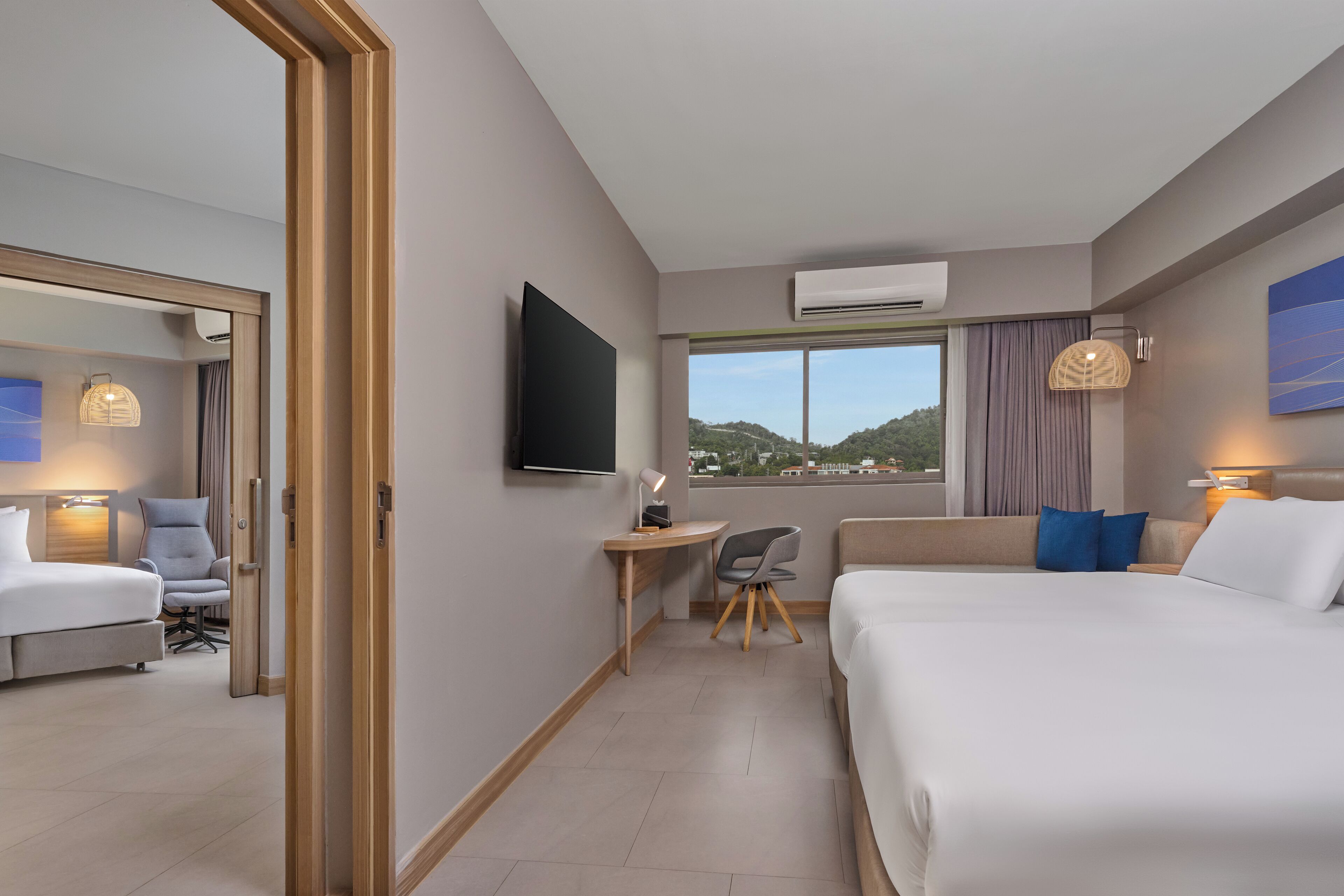 Habitación de hotel con cama, escritorio, silla, televisor y vistas al exterior.