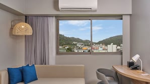 Una habitación moderna con sofá, escritorio y vista a un paisaje urbano a través de un ventanal grande.