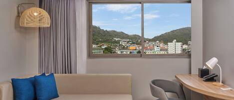 Una habitación moderna con sofá, escritorio y vista a un paisaje urbano a través de un ventanal grande.