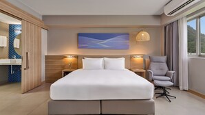Habitación de hotel moderna con una cama grande, lámparas de noche, una silla y vistas al exterior.