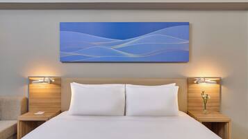 Een moderne hotelkamer met een groot bed, twee nachtkastjes met lampen, een kunstwerk aan de muur en een vaas met bloemen op een van de nachtkastjes.