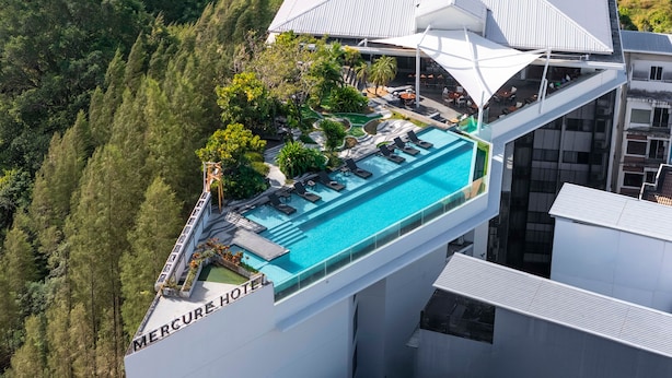 Un hotel de gran altura con piscina infinita en la azotea, rodeado de exuberante vegetación y arquitectura moderna.