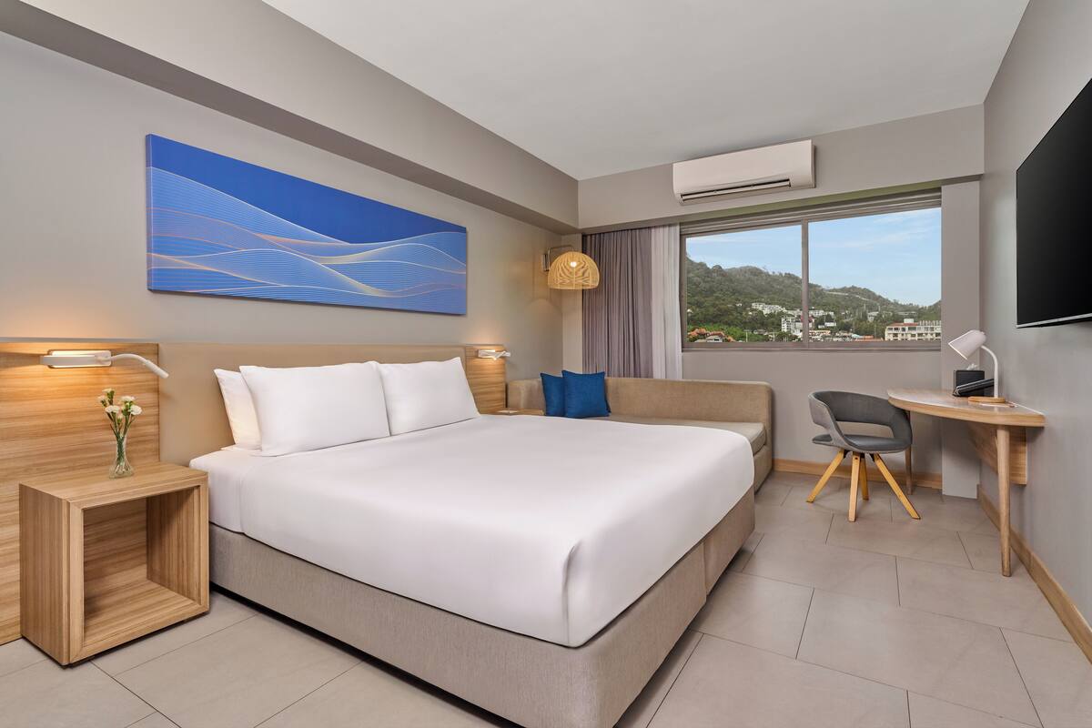 A modern hotel room with a large bed, a desk, and a view of the city.