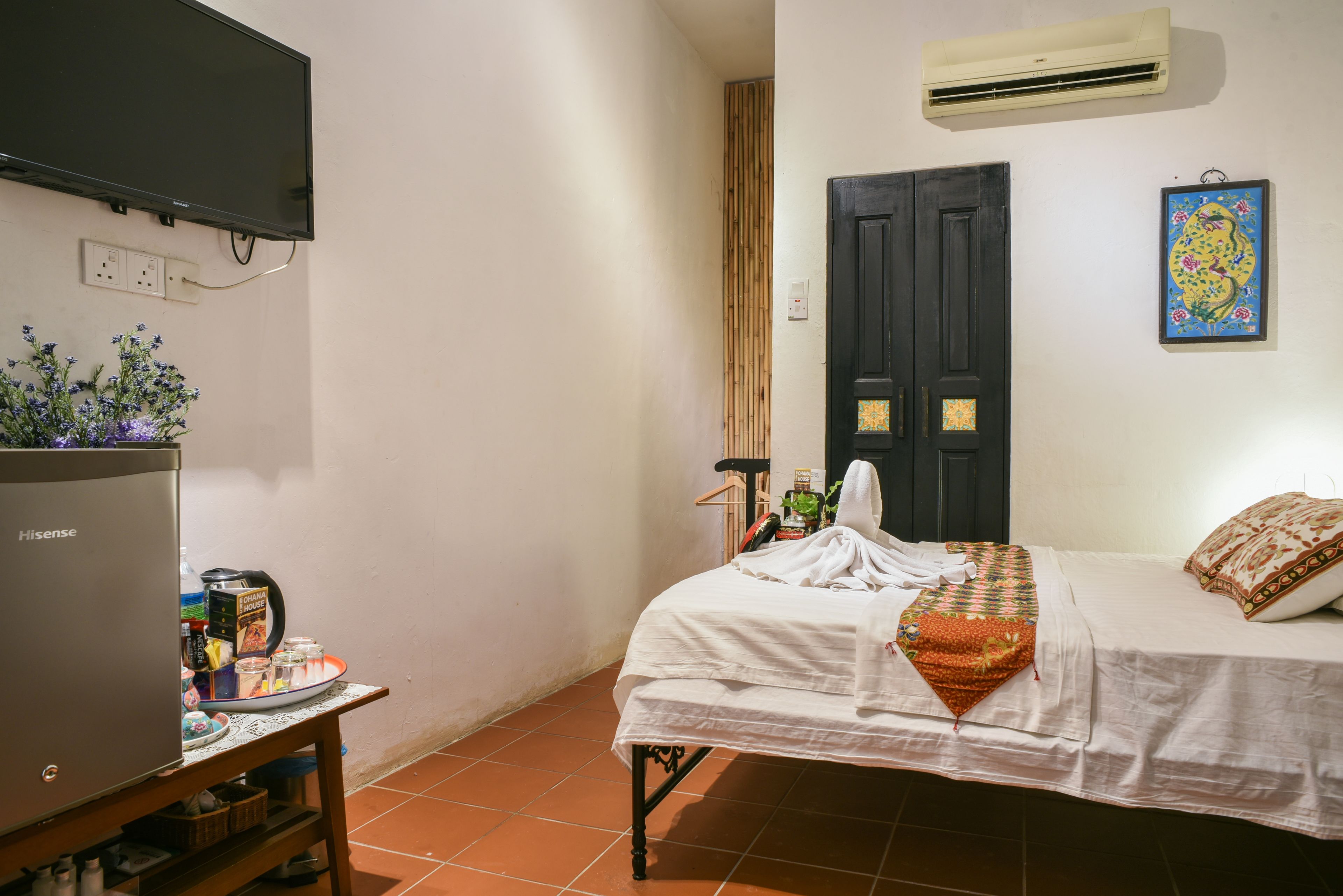 A bedroom with a bed, a TV, a table with items, and a wall-mounted air conditioner.