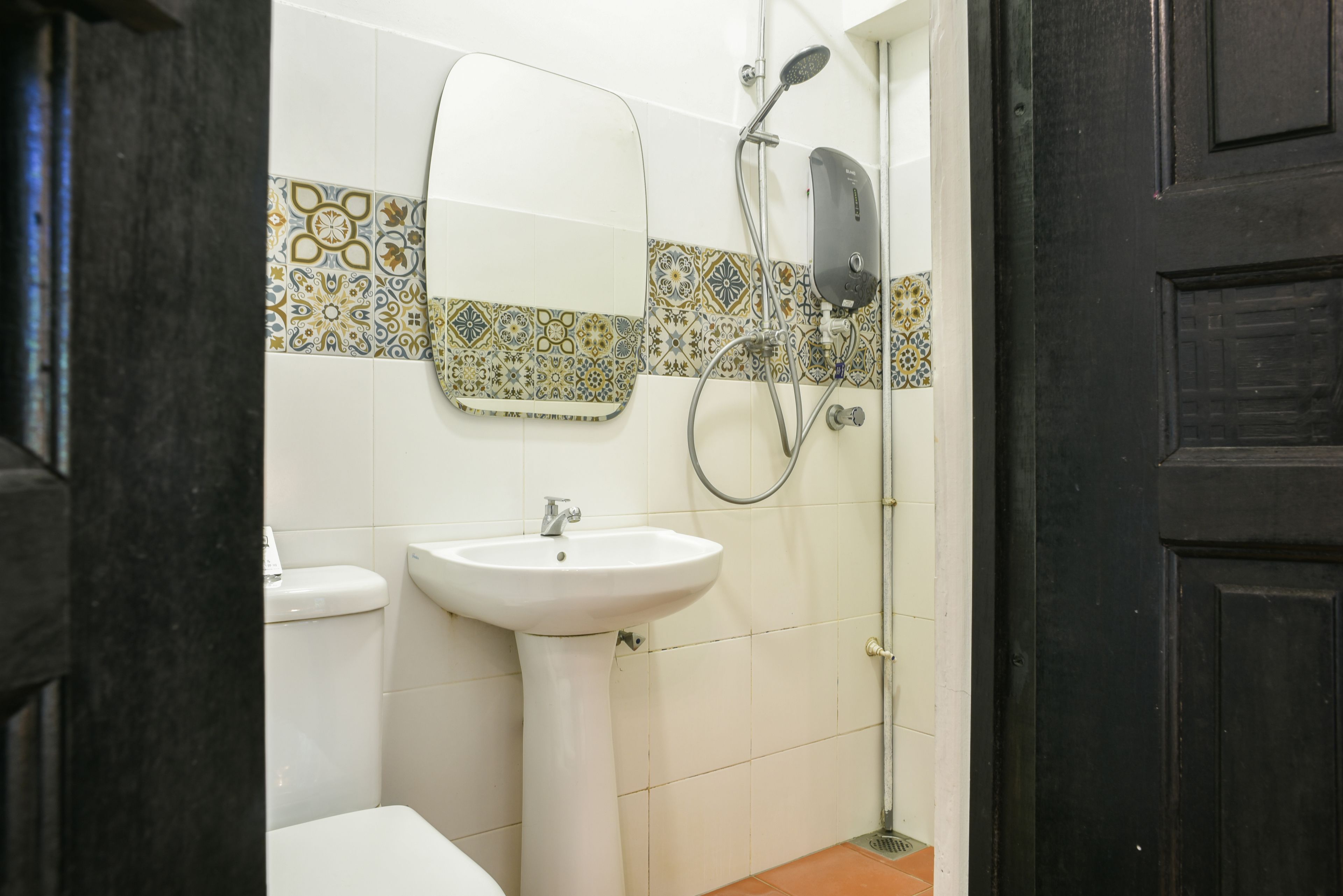 A bathroom with a white sink, a mirror, a shower with a handheld showerhead, and patterned tiles on the wall.