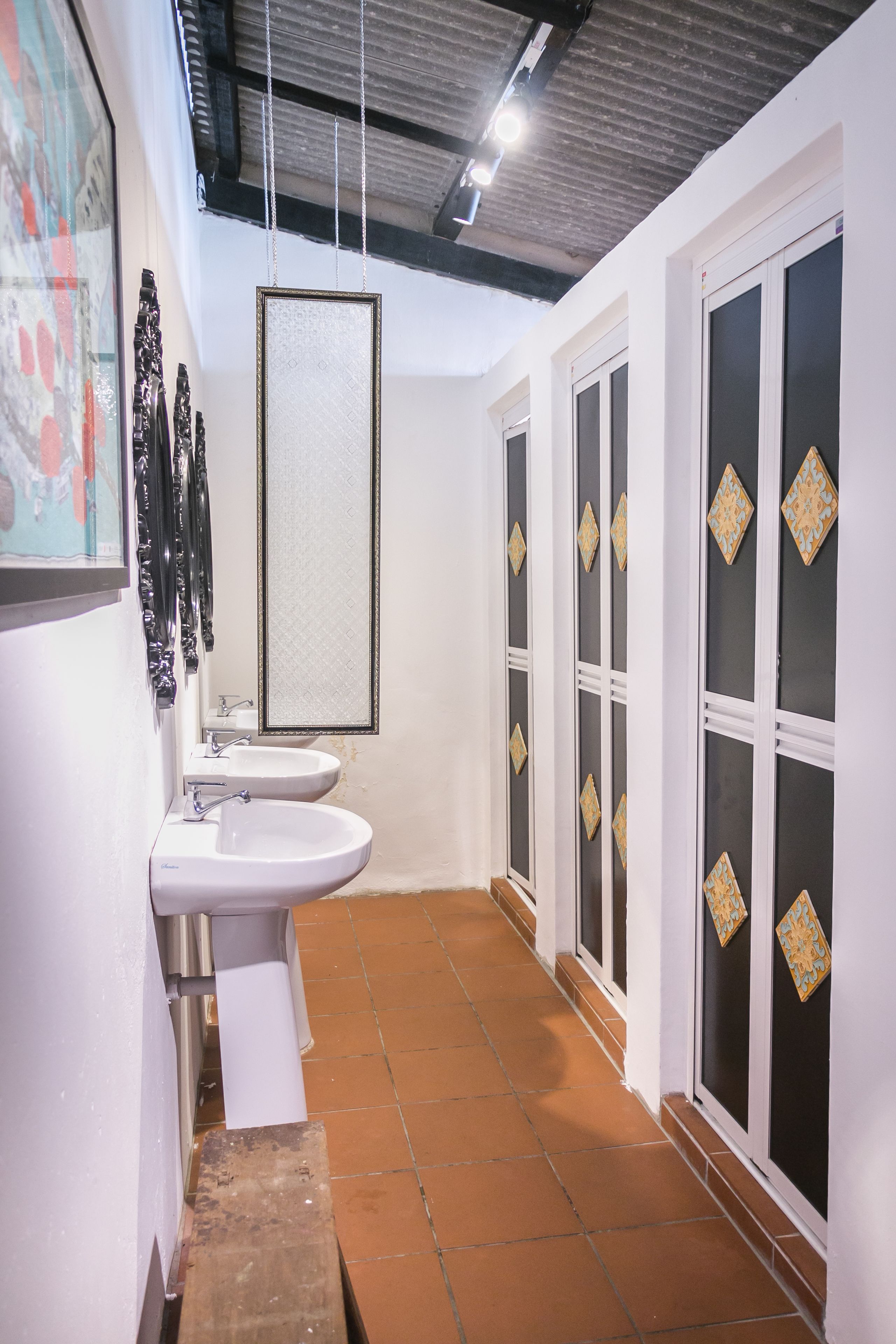 Un couloir étroit avec deux éviers, un miroir et une porte ornée de panneaux décoratifs.