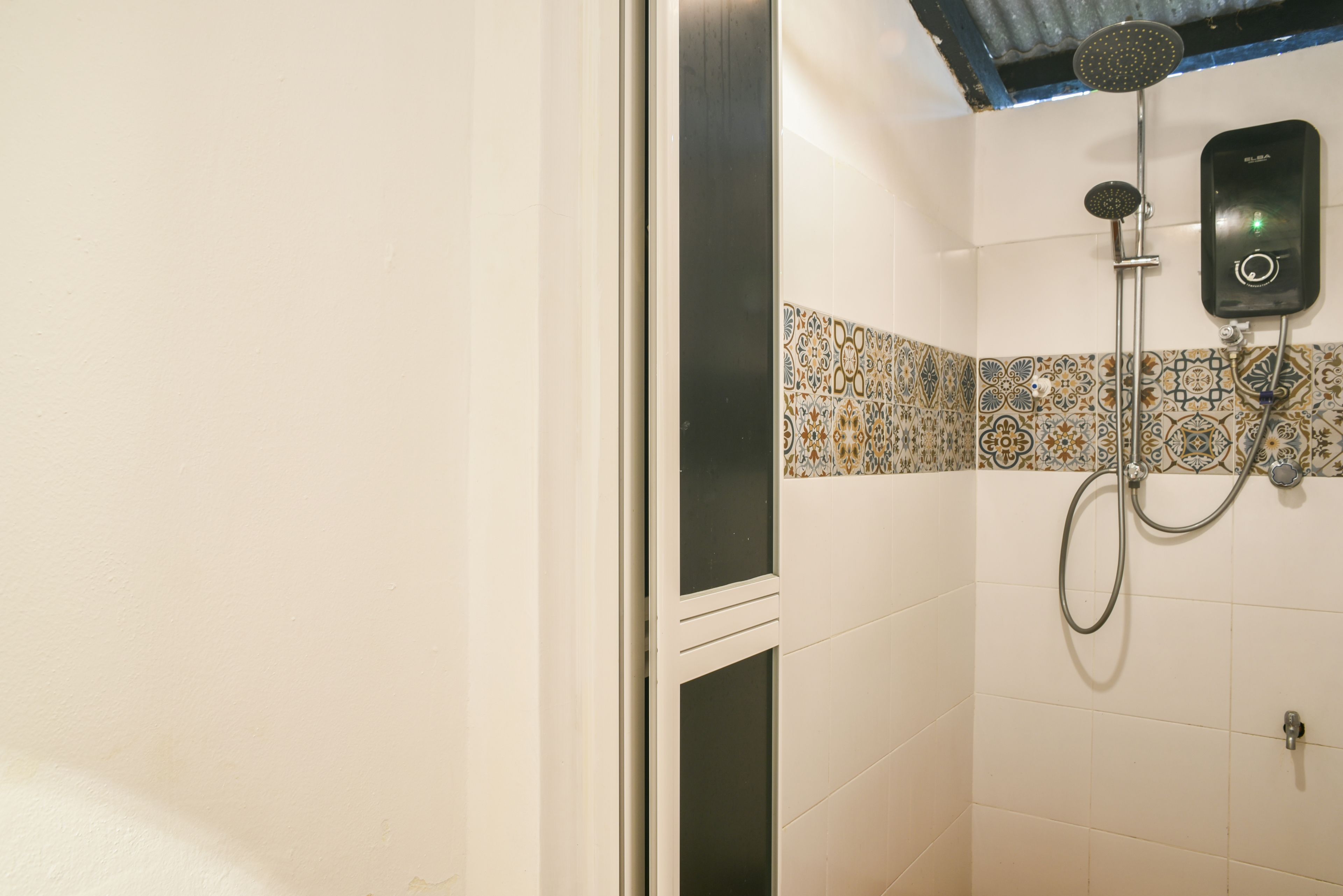 A shower area with a handheld showerhead and a wall-mounted control panel.