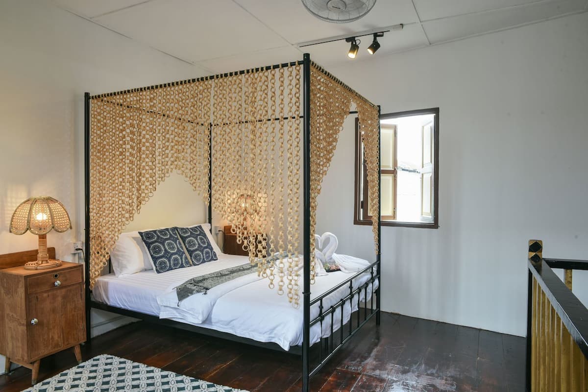 A four-poster bed with a canopy, a bedside table with a lamp, a wooden nightstand, and a patterned rug.