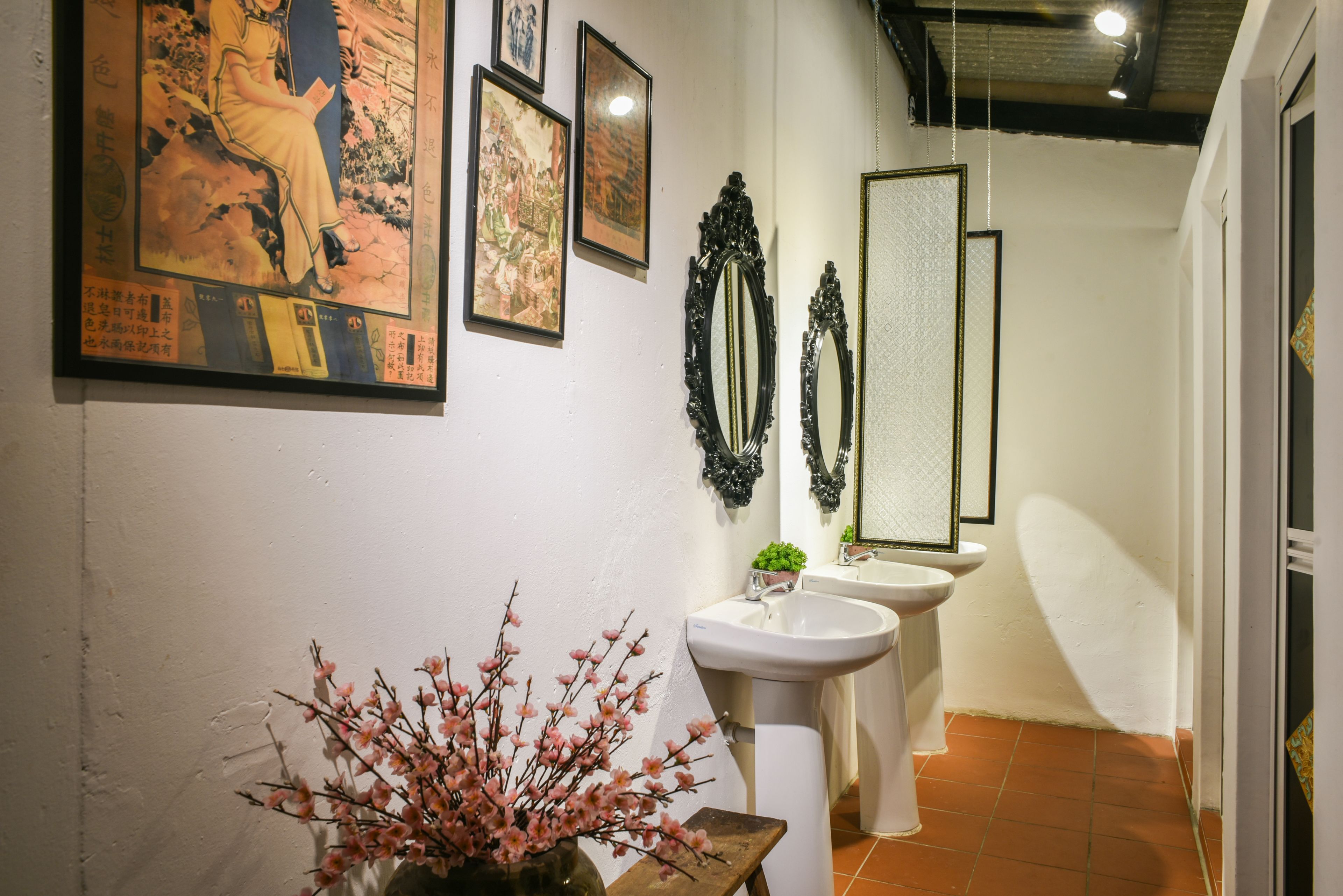 A narrow hallway with a white sink and pedestal, a mirror, and a vase with pink flowers.