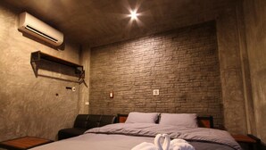 A hotel room with a brick wall, a bed with two pillows, a bedside table, and an air conditioning unit. - Paradiso Boutique Resort (Trat)