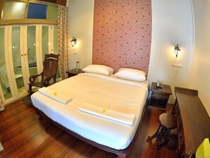 A hotel room with a large bed, a wooden chair, a desk with a telephone, and a wardrobe with glass doors. - Sleep Resort (Surat Thani)