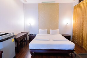 A hotel room with a large bed, a desk, a refrigerator, and a wall with a patterned design. - Sleep Resort (Surat Thani)