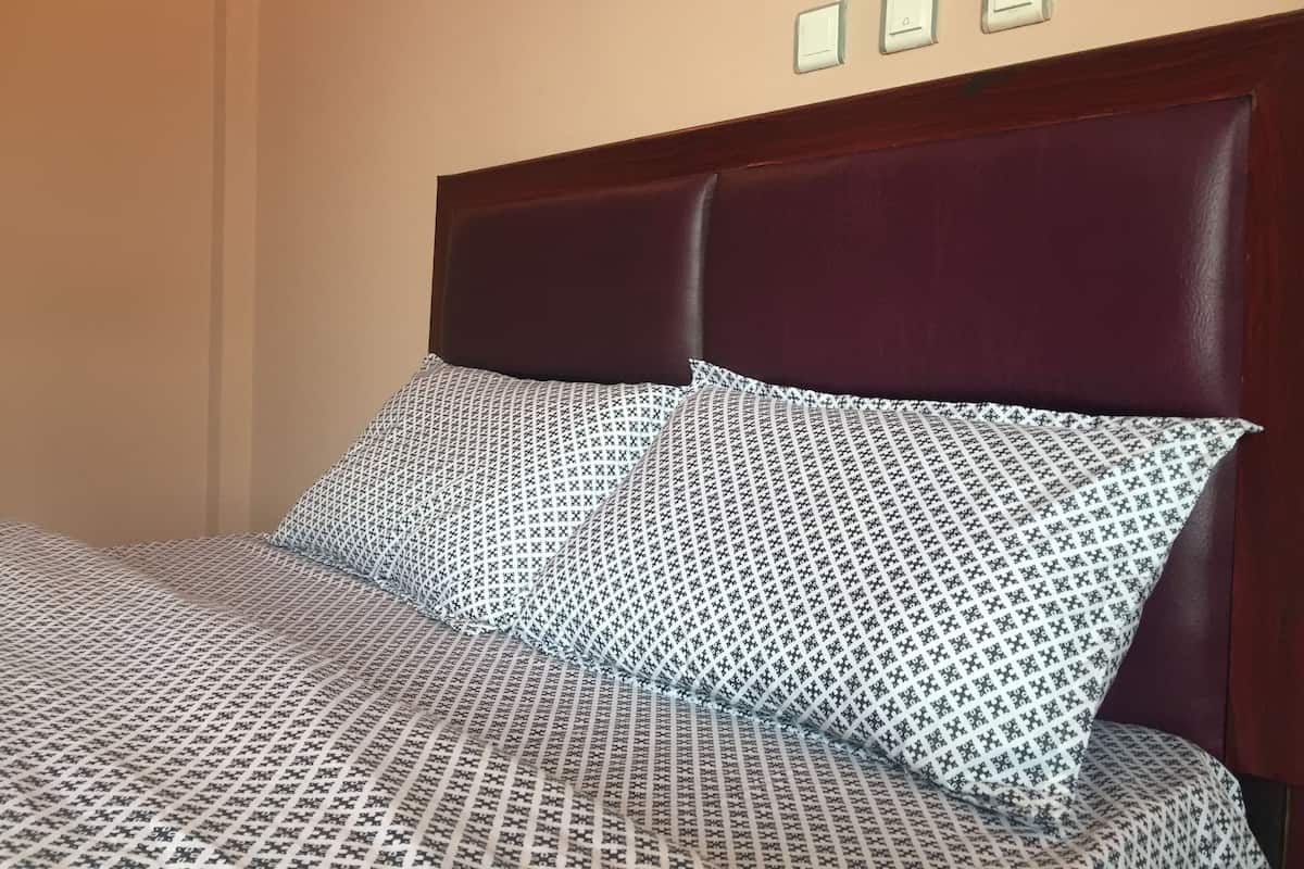 A bed with a patterned bedspread and two pillows, a wooden headboard, and three wall-mounted light switches.