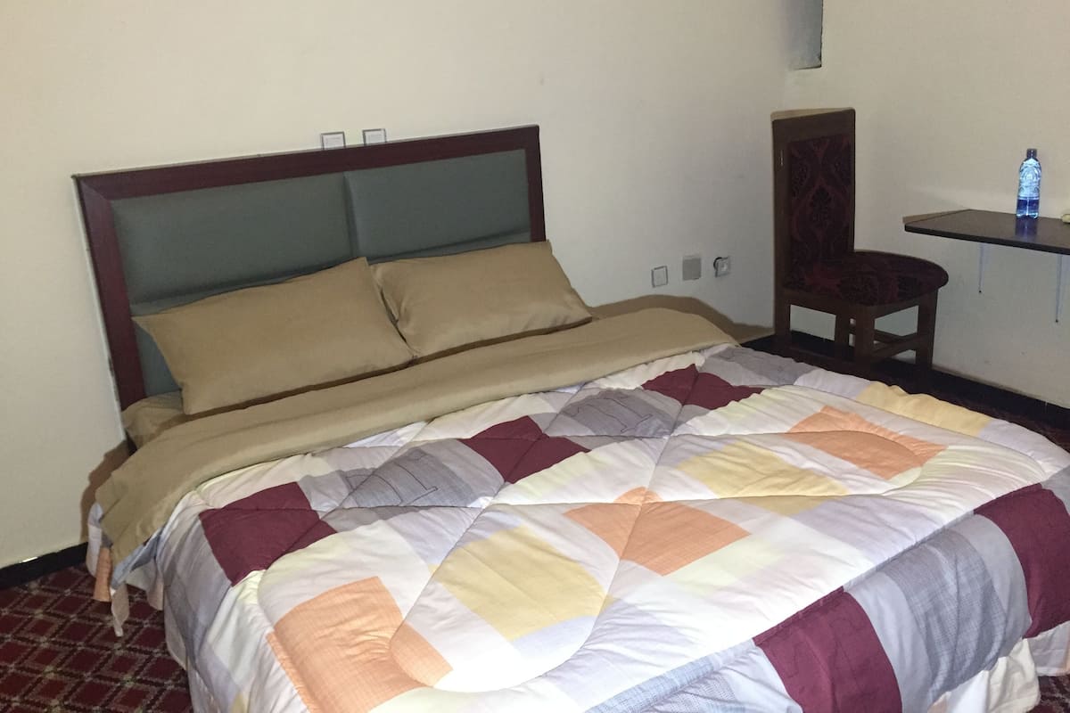 A neatly made bed with a patterned quilt, a wooden headboard, and a small bedside table with a water bottle.