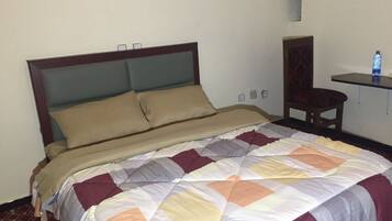Una cama bien hecha con colcha estampada, cabecera de madera y una mesita de noche con una botella de agua.