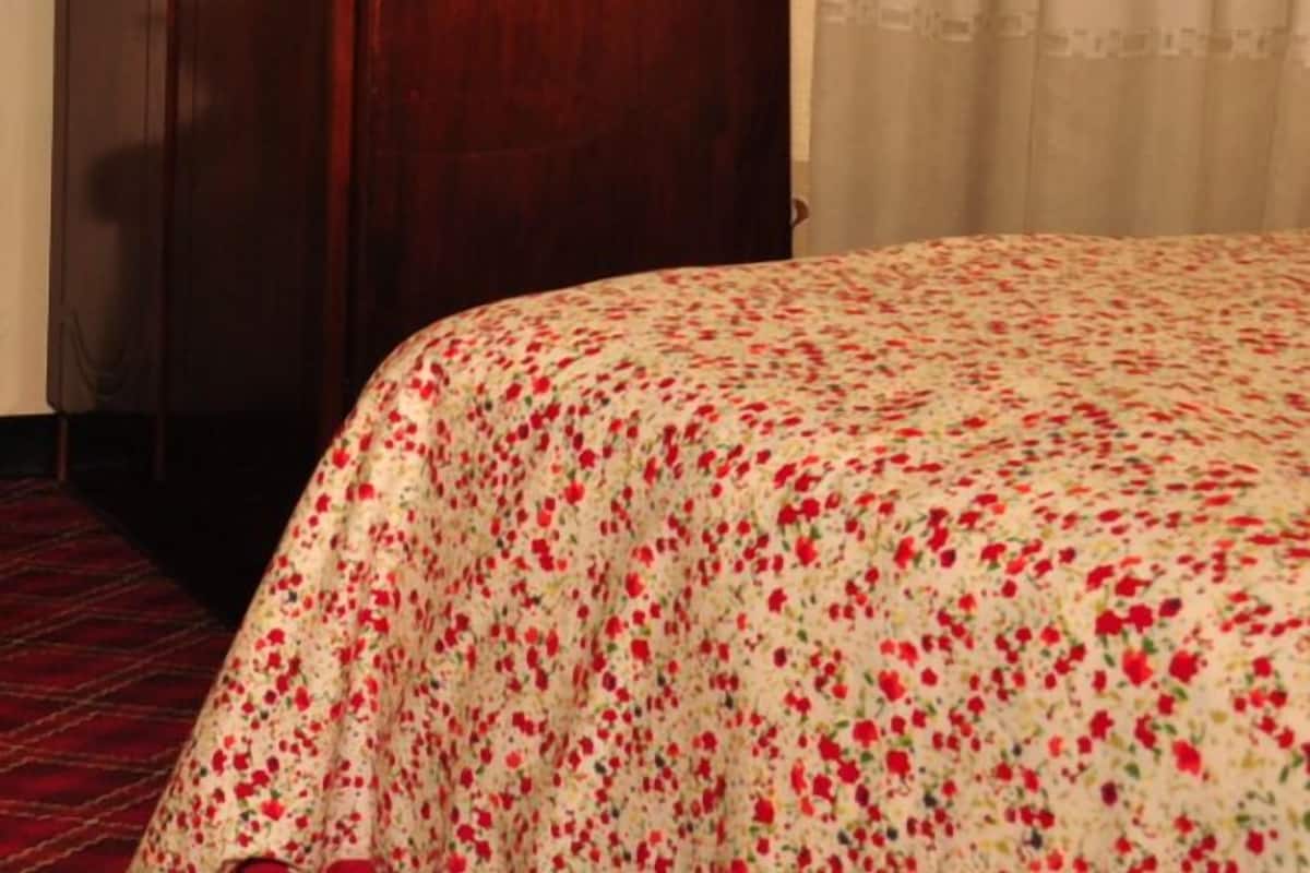 A bedroom with a wooden wardrobe, floral curtains, and a bed with a floral bedspread.