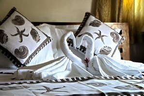 Un lit bien fait, avec des serviettes disposées en forme de nœud, des oreillers ornés de motifs marins et une tête de lit en bois.
