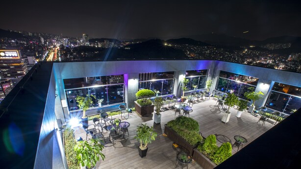 A rooftop terrace with multiple seating areas, potted plants, and a view of the cityscape at night. - CS Premier Hotel Seoul (Seoul)