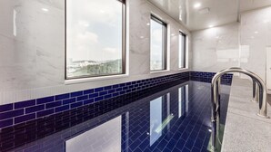 A modern indoor swimming pool with large windows, blue-tiled walls, and a clear view of the cityscape. - CS Premier Hotel Seoul (Seoul)