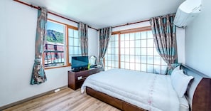 A bedroom with a bed, a TV, a dresser, and a window with curtains. - Sea Dragon Pension (Seogwipo)