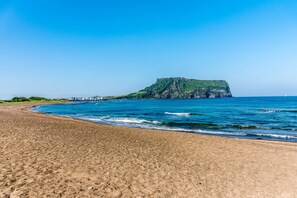 A beach with a large cliff and ocean. - Sea Dragon Pension (Seogwipo)